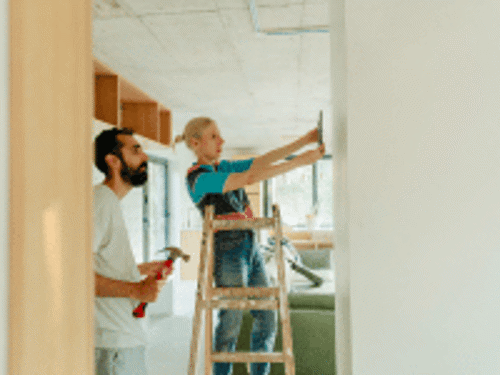 a couple trying to nail a picture frame to a wall